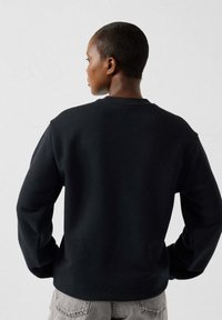 Sudadera negra hecha de tela suave, con cuello redondo, mangas largas y un ajuste relajado. Acabado texturizado sin patrones visibles.