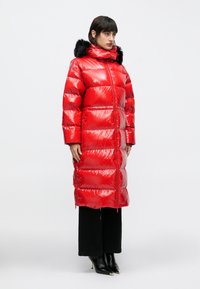 Piros, fényes felületű steppelt kabát, fekete műszőrme kapucnival, cipzáras záródással és hosszú ujjakkal. Vízszintes varrással és oldalzsebekkel rendelkezik.