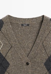 Brązowy sweter rozpinany z dekoltem w serek, pokryty ciemnobrązowymi cętkami, z ciemnoszarym i białym wzorem w romby oraz pojedynczym ciemnym guzikiem przy kołnierzu.