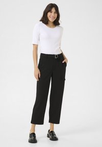Zwarte high-waisted broeken met wijde pijpen, een stoffen riem en zijzakken. Gepaard met een aansluitend wit T-shirt met korte mouwen en zwarte loafers.