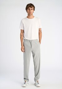 Vit kortärmad t-shirt, ljusgrå byxor med elastiskt midjeband, slätt tyg, bärs med vita sneakers, synliga tatueringar på armarna.