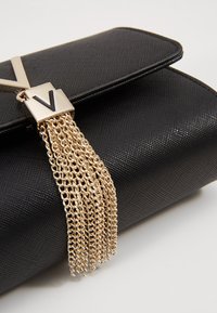 Black textured handbag with a gold chain tassel and a contrasting metallic clasp featuring a stylized "V." Features a sleek rectangular shape.