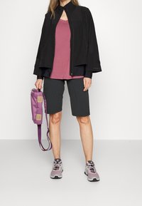 Svart jacka, rosa topp, mörka shorts och ljuslila väska. Jackan har en unik krage och ett flödande mönster; skorna är ljusgrå och lila.