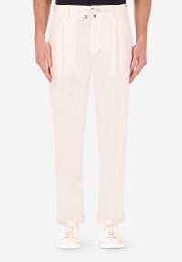 Pantaloni beige chiaro con frontale piatto, pieghe e vita elastica. Realizzati in un tessuto morbido, abbinati a sneakers bianche.