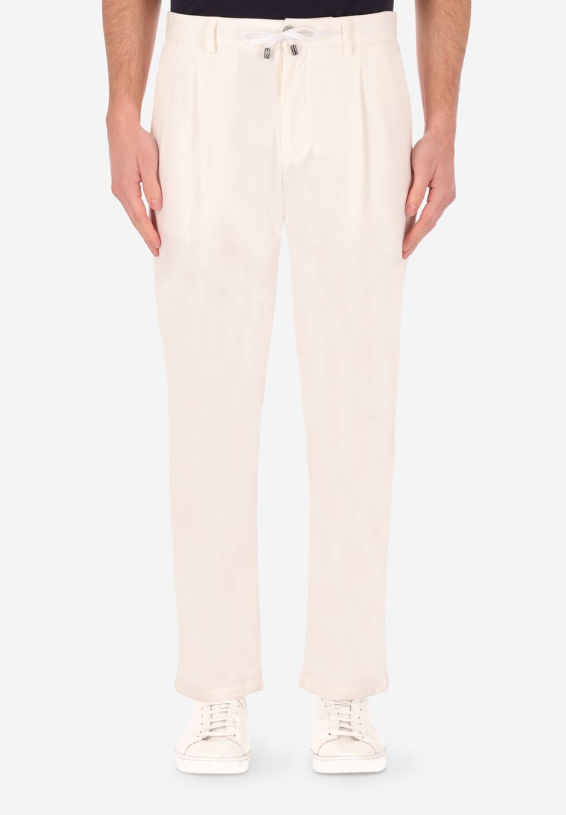 Pantaloni beige chiaro con frontale piatto, pieghe e vita elastica. Realizzati in un tessuto morbido, abbinati a sneakers bianche.