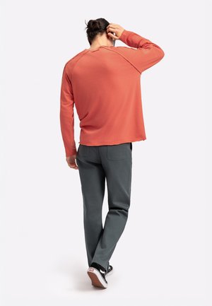 Langarmige, koraalkleurige shirt met een relaxte pasvorm en een afgeronde zoom. Gecombineerd met grijze broek en zwarte sneakers met witte accenten.