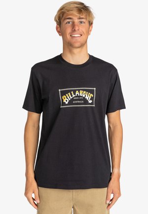 Black cotton t-shirt featuring a central logo patch with "Billabong" in yellow and white, crew neck, short sleeves, and relaxed fit.