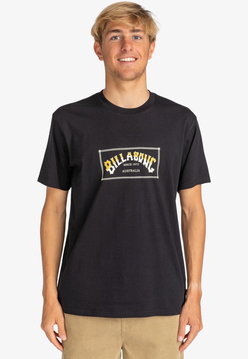 Black cotton t-shirt featuring a central logo patch with "Billabong" in yellow and white, crew neck, short sleeves, and relaxed fit.
