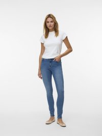 Balta kokvilnas T-krekls, piegulošs dizains, īsām piedurknēm. Zilas šauras piegriezuma džinsi ar gludu faktūru. Bēša krāsas dzīvokļi ar vienkāršu loku detaļu.