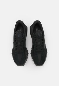 Ett par svarta New Balance-sneakers med mesh- och mockadetaljer, svarta snören och strukturerade gummisulor, visade ovanifrån på en vit bakgrund.