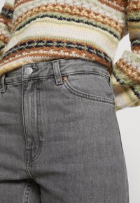 Los pantalones vaqueros grises de cintura alta cuentan con una textura suave, costuras sutiles, detalles en botón de cobre y un diseño de cinco bolsillos con un ajuste clásico.