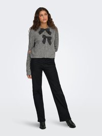 Gray knit sweater with two black satin bows at the neckline, paired with black wide-leg jeans and heeled black ankle boots.