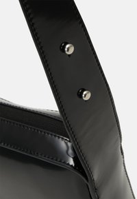 Borsa a mano in pelle verniciata nera con superficie liscia, una tracolla robusta con accessori in argento e cuciture dettagliate lungo i bordi.