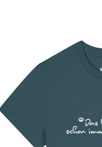 Teal katoenen t-shirt met een ronde hals en korte mouwen, met witte tekst in een handgetekende stijl. Gladde textuur zonder zichtbare logo's.