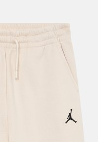 Bež jogger hlače s elastičnim pojasom i vezicom, s bočnim džepovima i crnim Jumpman logotipom na lijevom bedru.