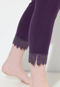 Fioletowe legginsy o dopasowanym kroju, z misterną koronkową lamówką przy kostkach i wycięciami. Miękki, elastyczny materiał o gładkiej fakturze.