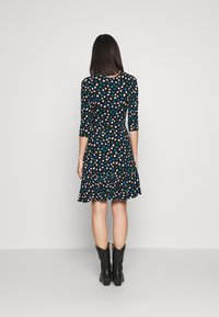 Uppblåst svart klänning med ett flerfärgat prickmönster, trekvartsärmar och en volangkant, kombinerad med svarta ankelskor.