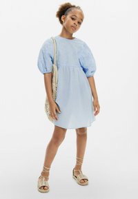 Světle modré šaty s nabíranými rukávy, vyšívaným korálkem a splývavou sukní. V kombinaci s tkanou taškou a sandály na pásky. Hladká látka.