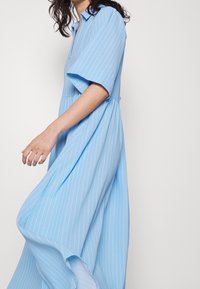 Ljust blårandig klänning med korta ärmar, krage och en flödande design som når anklarna. Mjuk textur och löst passform för komfort.