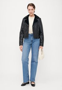 Black leather cropped jacket with faux fur collar, paired with light blue straight-leg jeans and black flats, holding a small white bag.