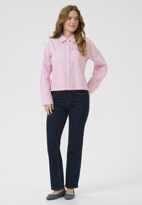 Camicia a righe rosa e bianche con colletto, dotata di taschino sul petto. Indossata con jeans dritti blu scuro e ballerine blu.