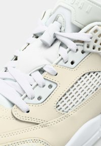 Világos bézs színű sneaker fehér fűzős, hálós betétekkel és textúrált felülettel; különleges középső fűzőzárat és márkázási részletet tartalmaz.