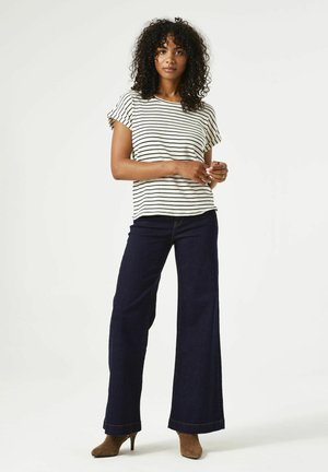 T-shirt en coton rayé à manches courtes, associé à un jean en denim foncé à large jambe. Des talons marron viennent compléter la tenue.