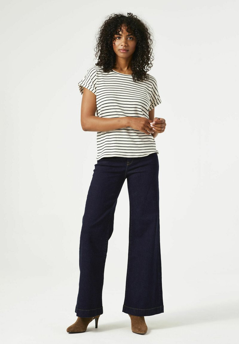 Camiseta de algodón a rayas con mangas cortas, combinada con pantalones vaqueros de pierna ancha en denim oscuro. Tacones marrones complementan el conjunto.