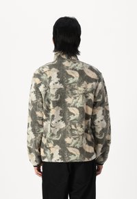 Fleece jacket with high collar; features a camouflage pattern in green, beige, and black; soft texture; fitted cut with a hemmed bottom.