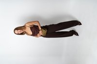 Hnedý top bez rukávov s prekladaným dizajnom, doplnený o tmavé nohavice s vysokým pásom a lodičky s špicatou špičkou. Drží malú olivovo zelenú kabelku.