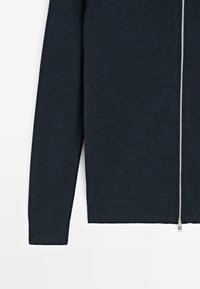 Pull en maille côtelée bleu marine foncé à manches longues avec fermeture éclair argentée pleine longueur à l’avant, présenté de la manche jusqu’au milieu du torse sur fond blanc.