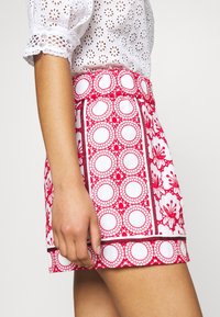 Jupe à motifs rouges et blancs avec des motifs circulaires et des accents floraux, dotée d'une coupe ajustée et d'une ceinture visible avec des détails de bordure.