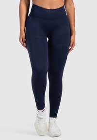 Leggings navy a vita alta realizzati in un tessuto morbido ed elastico. Presentano una larga cintura elastica e un branding discreto sull'anca.