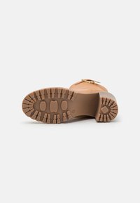 Bota de goma color marrón claro con una suela texturizada, que presenta un empeine liso, un detalle de hebilla en el costado y un diseño de puntera redondeada.