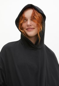 Svart huva sweatshirt med lös passform, som har en funnel-neck, slät textur och minimalistisk design.