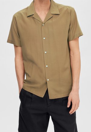 Chemise à manches courtes, de couleur vert olive, avec un col, affichant un devant à boutons et un tissu doux et lisse. Les boutons sont bleu clair.