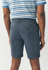Pantalones cortos grises con una textura suave, que cuentan con dos bolsillos traseros con botones negros. El dobladillo está enrollado para un aspecto casual.