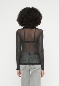 Top nero a maniche lunghe trasparente con una texture fine e glitterata, caratterizzato da un design aderente e da cinghie sul retro, abbinato a jeans grigio chiaro a vita alta.