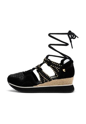 Sandale noire avec un dessus tissé, des accents en daim et un talon compensé en jute. Présente des brides croisées et des lacets spirales s'étendant vers le haut.