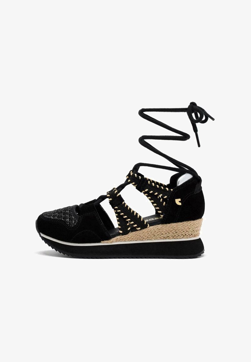 Sandalia negra con parte superior trenzada, acentos de ante y un tacón en cuña envuelto en yute. Presenta correas entrecruzadas y cordones en espiral que se extienden hacia arriba.
