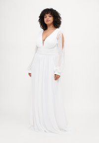 Weißes Maxikleid mit langen, transparenten Ärmeln, tiefem V-Ausschnitt, gerafftem Oberteil und fließendem Stoff, der eine weiche, glatte Textur aufweist.