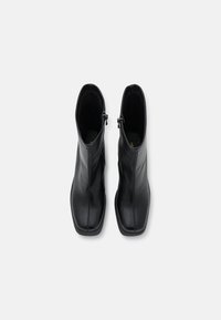 Bottes cheville en cuir noir à finition lisse, avec des détails de coutures verticales et des fermetures éclair sur le côté extérieur pour un enfilage facile. Semelles plates.