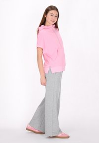 Felpa corta con zip rosa a maniche corte e tasca frontale, abbinata a pantaloni della tuta grigi larghi. La calzatura presenta dettagli rosa e una suola piatta.