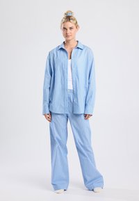 Light blue striped pajama set with orange stripes. Button-up shirt, relaxed fit. Loose pants with an elastic waistband. Soft fabric texture.