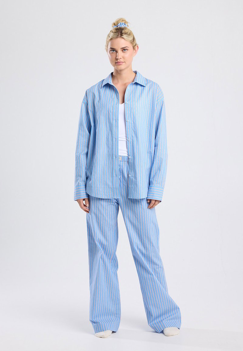 Light blue striped pajama set with orange stripes. Button-up shirt, relaxed fit. Loose pants with an elastic waistband. Soft fabric texture.