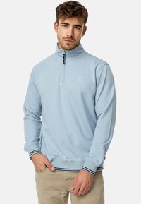 Lys blå kvart-zip sweatshirt med en sort lynlås, ribbede manchetter og kant med marineblå striber. Blødt stof med en diskret logodetalje.
