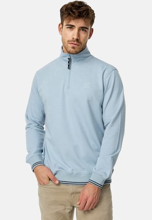 Ljusblå kvartdraget sweatshirt med en svart dragkedja, ribbade mudd och nederkant med marinblå ränder. Mjuk tyg med en subtil logodetalj.