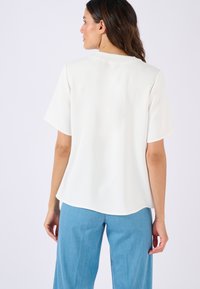 Blusa bianca a maniche corte con scollo rotondo, texture liscia e vestibilità rilassata, abbinata a jeans a gamba larga azzurri.