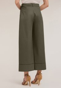 Brede, olijfgroene broeken met een hoge taille en uitsnijdingen aan de onderkant, gecombineerd met tan kleurige hoge hakken met banden.