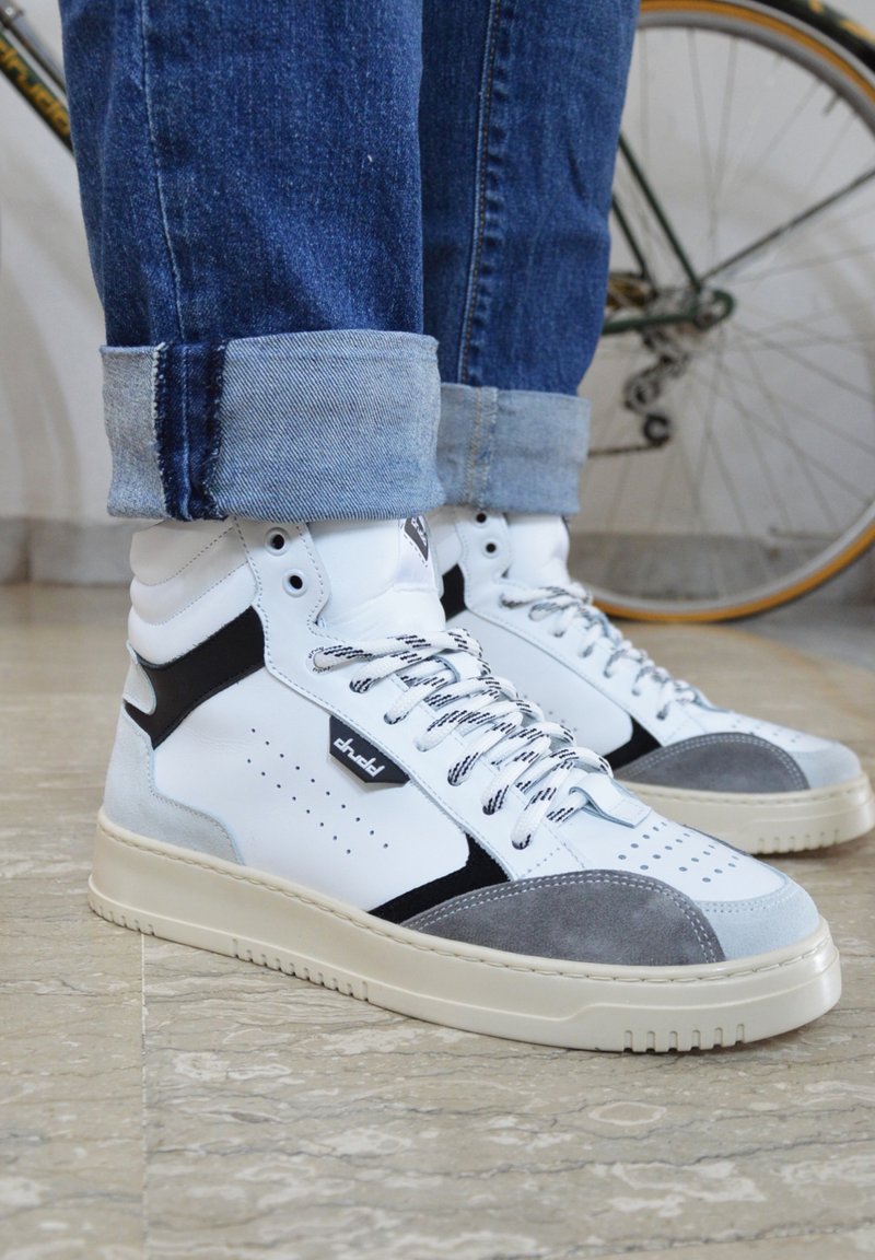 Zapatillas altas con parte superior de cuero blanco, acentos de ante gris, detalles en negro y cordones texturizados. Suela de goma crema gruesa.